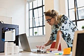 Female designer working at laptop next to 3D printer