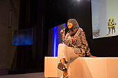 Smiling female speaker with microphone in hijab on stage