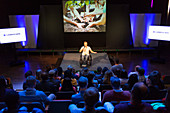 Audience watching female speaker in wheelchair on stage