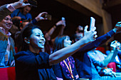 Enthusiastic woman using camera phone in dark audience