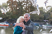 Playful senior couple taking selfie at pond in park