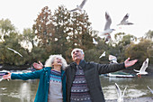 Playful senior couple watching flying birds at pond in park