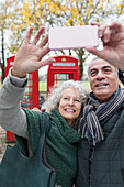 Senior couple taking selfie in front of red telephone booths