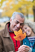 Affectionate senior couple holding orange autumn leaf