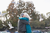Affectionate senior couple hugging in park with flying birds