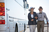 Smiling active senior couple tourists walking along bus