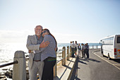 Senior couple tourists hugging at sunny ocean overlook