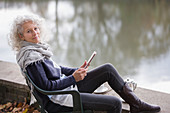 Active senior woman using digital tablet at park pond