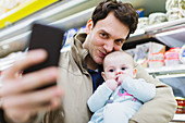 Father and baby daughter taking selfie in supermarket