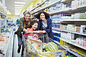 Playful women pushing shopping cart in supermarket aisle