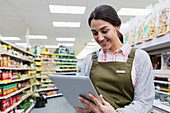 Female grocer using digital tablet in supermarket aisle