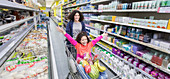 Mother pushing daughter in shopping cart in supermarket