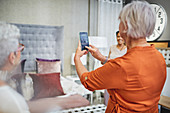 Woman with smart phone photographing bed in home decor shop
