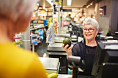 Senior female cashier helping customer at grocery checkout