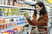 Young woman reading label on container in supermarket