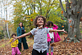 Carefree boy playing in autumn leaves with family in woods