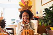 Portrait happy girl with turkey hat carving pumpkin at table