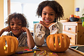 Portrait happy brother and sister carving pumpkins at table