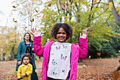 Portrait happy girl throwing autumn leaves overhead in woods