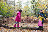 Mother and daughters walking on fallen log in autumn woods
