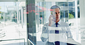 Businessman talking on cell phone at office window