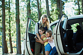 Mother hugging daughters outside car in woods