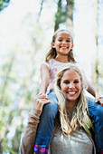 Mother carrying daughter on shoulders in woods