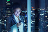 Smiling businesswoman checking cell phone in urban window