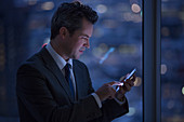 Businessman text messaging with cell phone in window