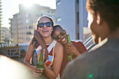 Happy young women friends drinking beer on sunny rooftop