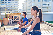 Young man and woman practicing yoga on sunny urban rooftop