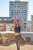 Young woman practicing yoga tree pose on sunny urban rooftop