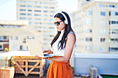 Woman with headphones and laptop working on urban rooftop