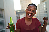 Portrait happy young woman drinking beer on urban balcony