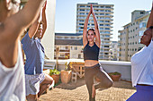 Friends practicing yoga tree pose on sunny rooftop balcony