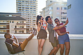 Young friends taking selfie on sunny urban balcony rooftop