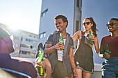 Happy young friends drinking beer on sunny urban balcony