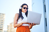 Young woman with headphones using laptop on urban balcony