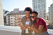 Happy young couple using smart phone on rooftop balcony