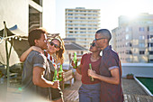 Friends drinking beer on sunny urban rooftop balcony