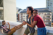 Happy young couple laughing and hugging on sunny balcony