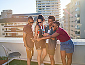 Happy young friends with smart phone on sunny urban balcony