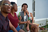 Confident young man drinking beer with friends on patio