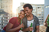 Happy young couple drinking beer on sunny rooftop balcony