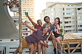 Carefree young friends drinking beer on rooftop balcony