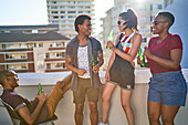 Happy young friends drinking beer on sunny rooftop balcony