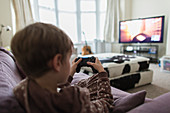 Boy playing video game on living room sofa