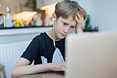 Focused boy with headphones using laptop in kitchen