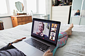 Woman with laptop video chatting with friends on bed