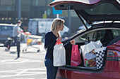 Woman loading groceries into back of car in parking lot